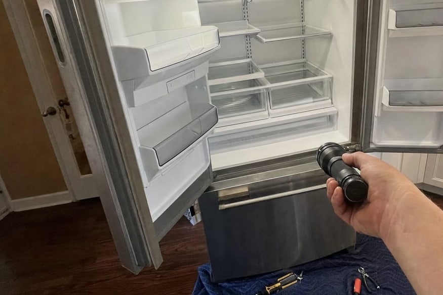 Built-in refrigerator door held open while a flashlight is played over the interior shelves