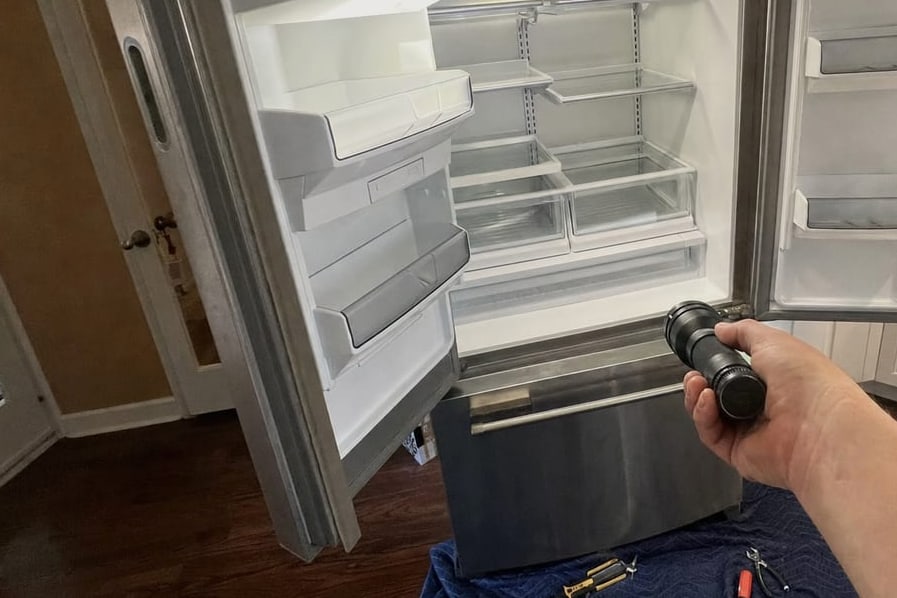 Open built-in refrigerator with a flashlight held on the empty interior during a diagnosis