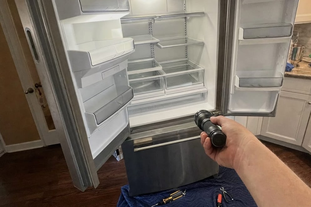 Built-in refrigerator open with its shelves empty and a work light held on the interior
