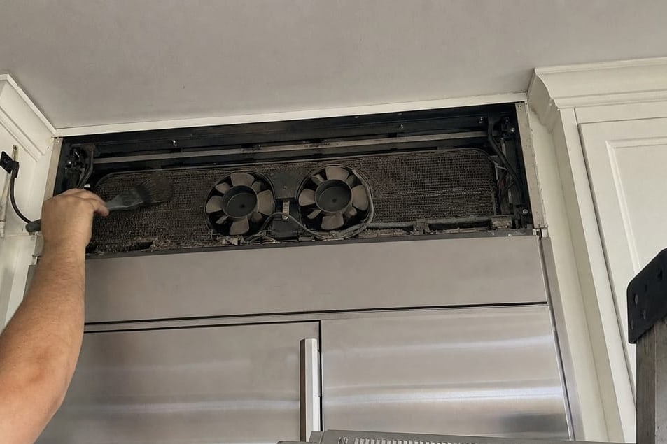 Condenser fans and coil visible behind the opened upper grille panel of a built-in refrigerator