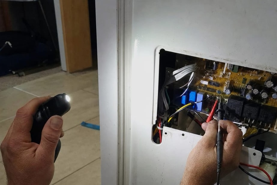 Multimeter probes held on the terminals of an appliance control board in its housing