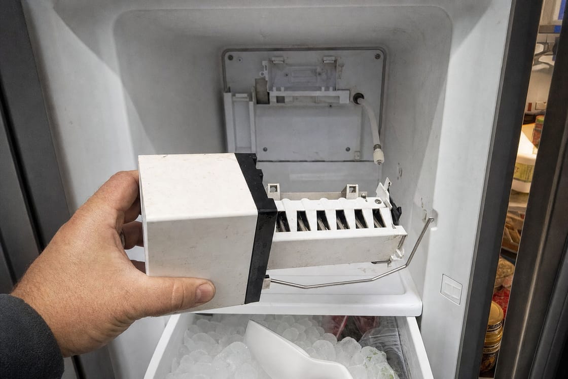 Ice maker module held out of its bay in the freezer wall with the mounting bracket and fill tube behind it