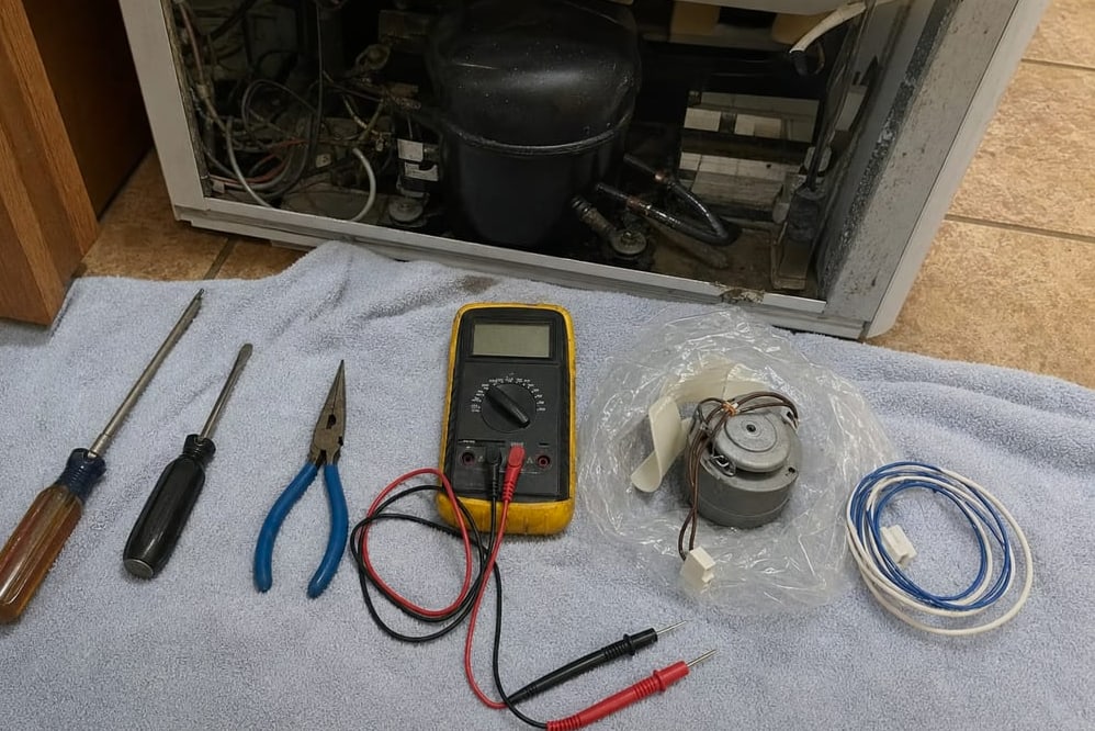 Screwdrivers, pliers, a multimeter and a coiled line laid out on a mat in front of a built-in refrigerator