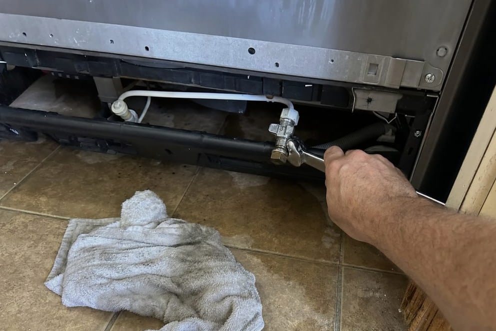 Water supply line and shut-off fitting at the base of a built-in refrigerator being turned with a wrench
